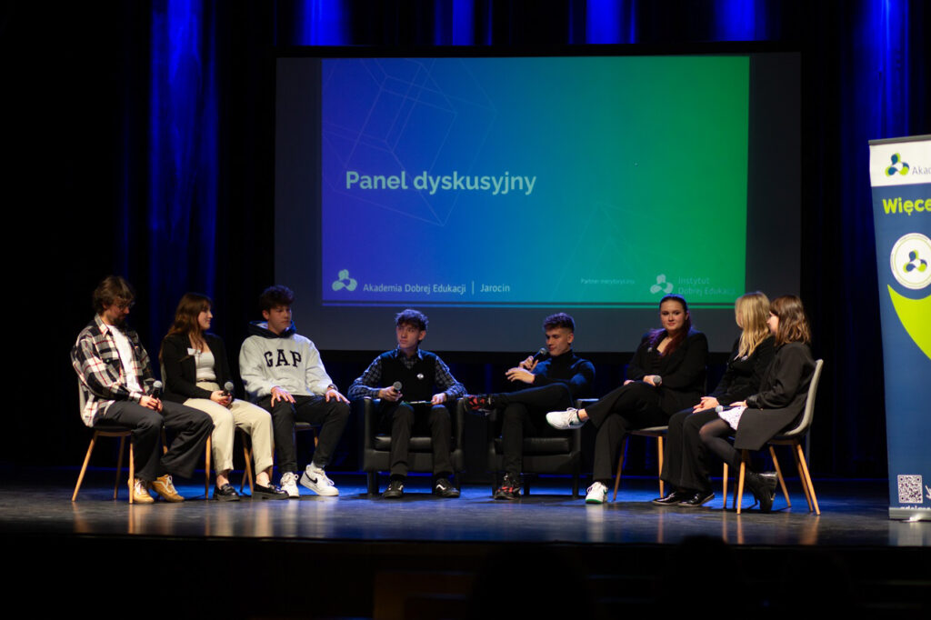 Uczniowie siedzą na scenie podczas panelu dyskusyjnego.
