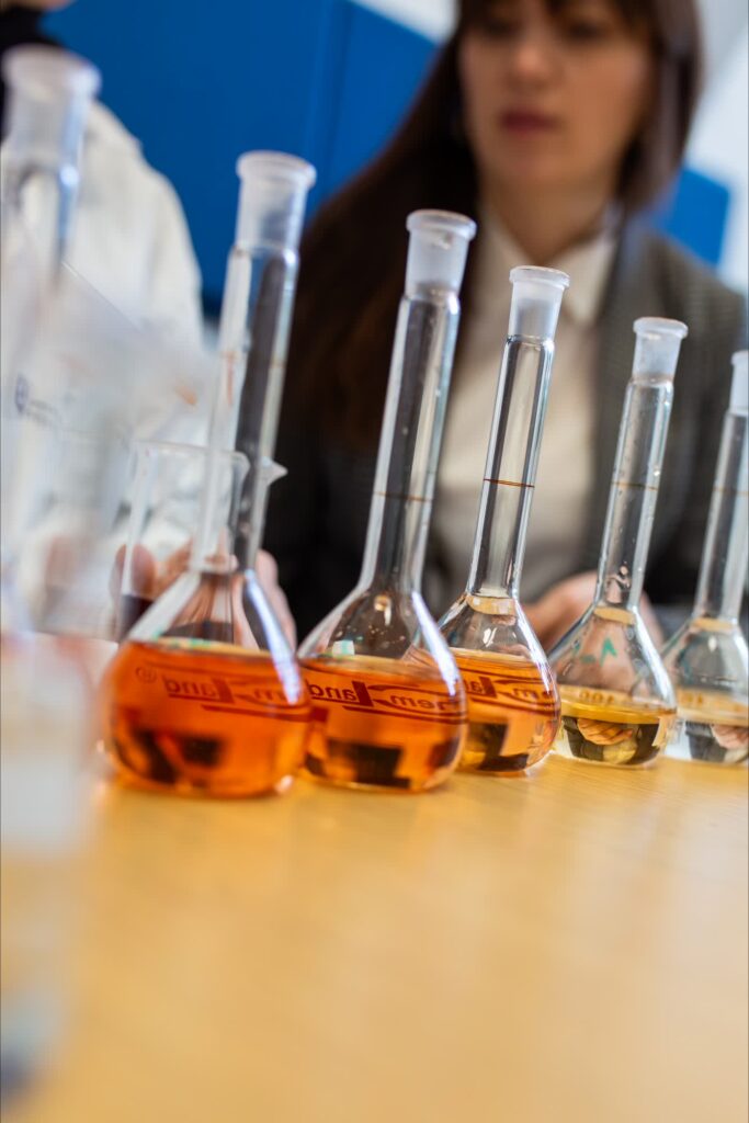 Rząd szklanych kolb stożkowych wypełnionych pomarańczowym roztworem chemicznym na stole laboratoryjnym.